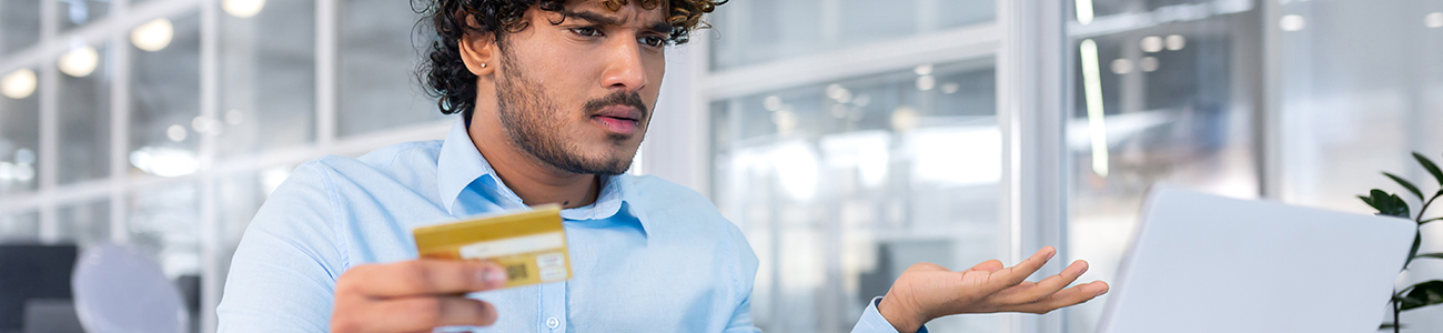 Man confused holding gift card looking at laptop