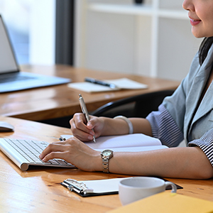 Cropped shot young female office worker working with computer and making notes on notebook