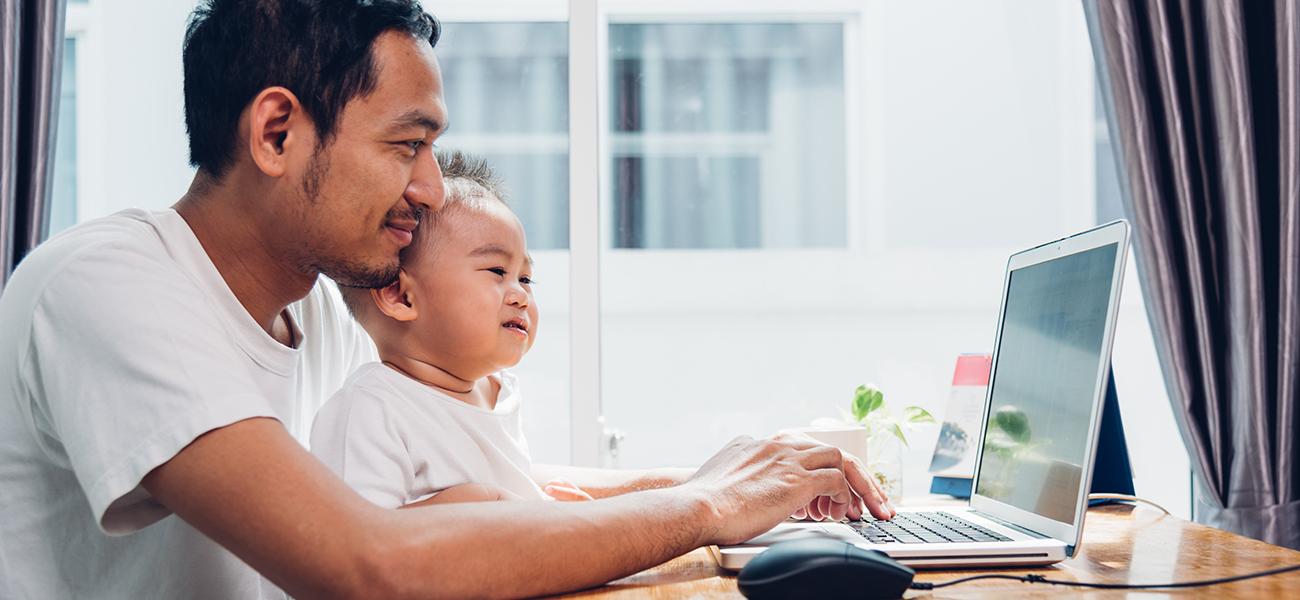 Father entering password on laptop with baby in lap