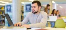 Middle aged man reading books and working on laptop in public library